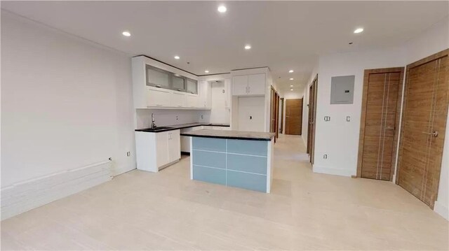 kitchen featuring electric panel, white cabinetry, a center island, and sink