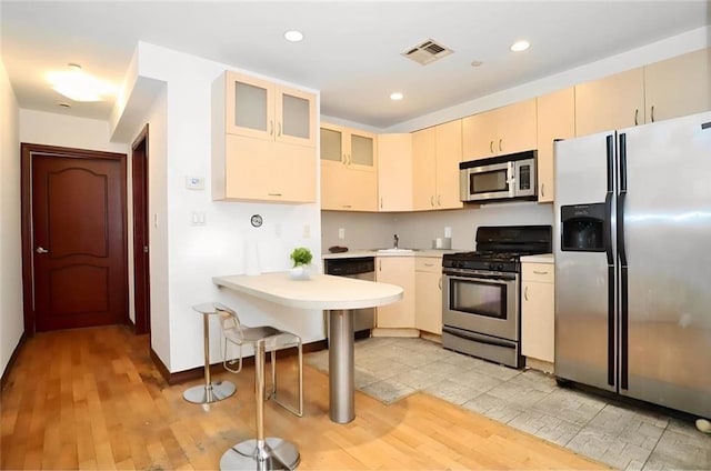 kitchen featuring visible vents, stainless steel appliances, light countertops, glass insert cabinets, and light wood-type flooring