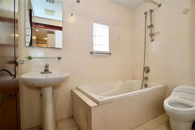 bathroom featuring tile patterned flooring, tiled shower / bath combo, tile walls, toilet, and tasteful backsplash