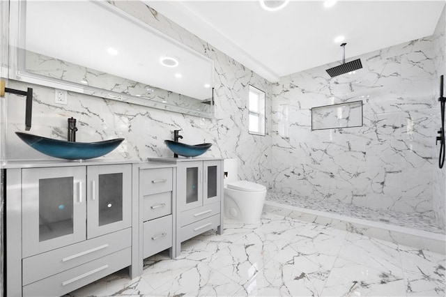 full bathroom with marble finish floor, a marble finish shower, double vanity, toilet, and stone wall