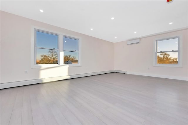 spare room featuring a healthy amount of sunlight, a wall mounted air conditioner, and light hardwood / wood-style flooring