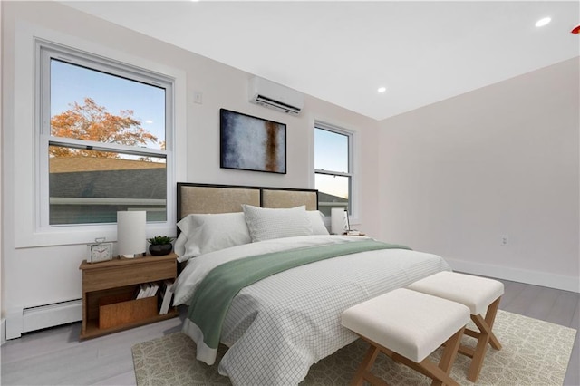 bedroom featuring a wall mounted AC, a baseboard heating unit, and light hardwood / wood-style flooring