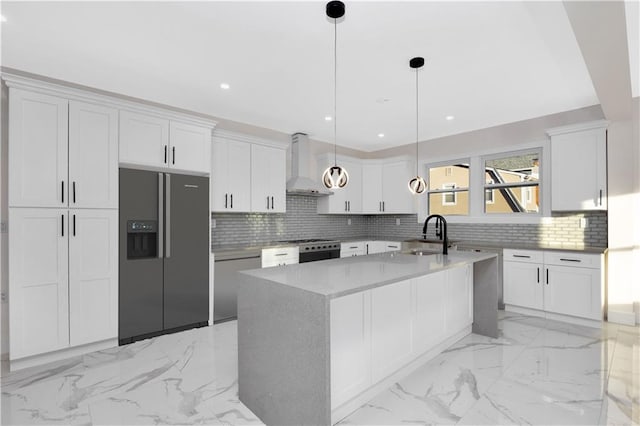 kitchen featuring marble finish floor, black refrigerator with ice dispenser, hanging light fixtures, a sink, and wall chimney exhaust hood