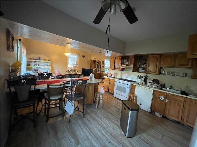 kitchen featuring ceiling fan, pendant lighting, a kitchen island, a breakfast bar, and white appliances