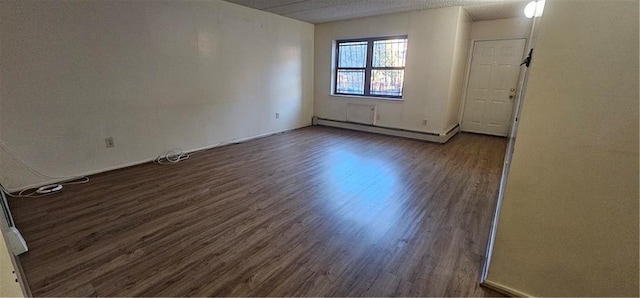 spare room featuring a baseboard heating unit and dark wood-type flooring