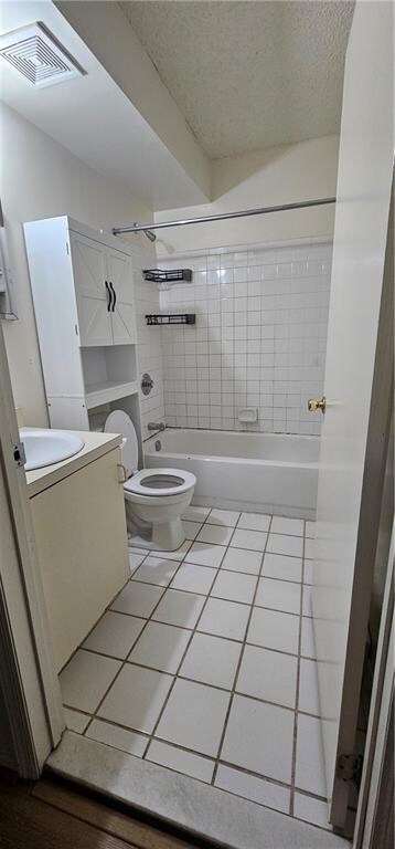 full bathroom featuring tiled shower / bath combo, vanity, tile patterned flooring, toilet, and a textured ceiling