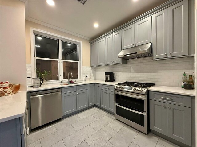 kitchen with appliances with stainless steel finishes, decorative backsplash, sink, ornamental molding, and gray cabinetry