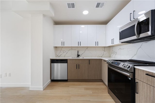 kitchen featuring appliances with stainless steel finishes, backsplash, white cabinets, and light wood-type flooring