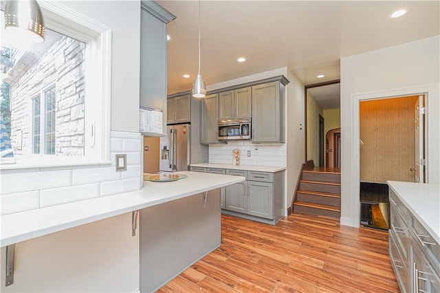 kitchen featuring light wood-style flooring, appliances with stainless steel finishes, light countertops, gray cabinets, and backsplash