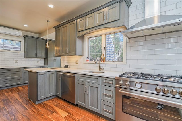 kitchen featuring a sink, stainless steel appliances, wall chimney exhaust hood, backsplash, and gray cabinetry