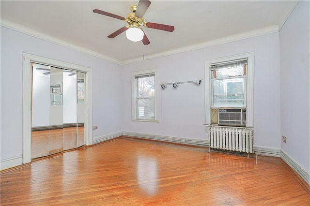 empty room with radiator, cooling unit, a ceiling fan, ornamental molding, and wood finished floors