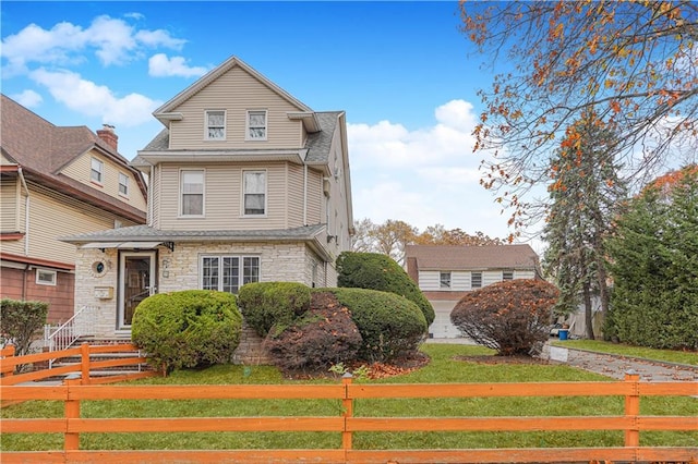 view of front of property with a fenced front yard, a front yard, stone siding, and a shingled roof