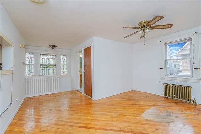 unfurnished room featuring a ceiling fan, radiator, a healthy amount of sunlight, and light wood-style floors