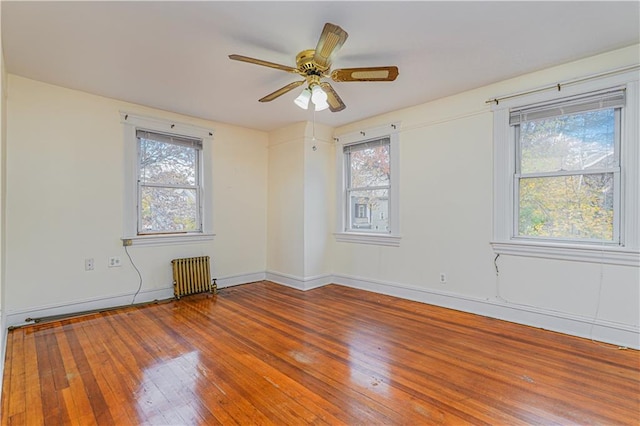 empty room with wood-type flooring, radiator heating unit, a ceiling fan, and baseboards