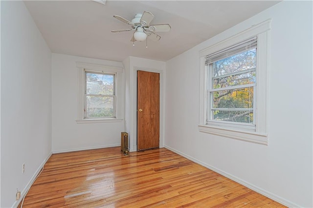 unfurnished room featuring radiator heating unit, light wood-style flooring, baseboards, and ceiling fan