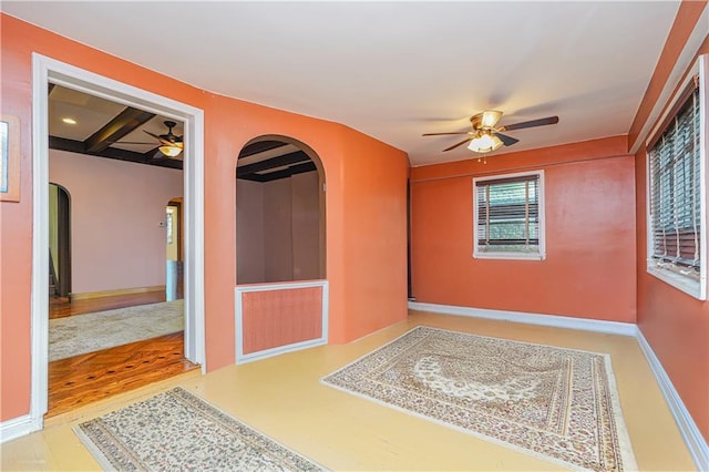empty room with coffered ceiling, arched walkways, beam ceiling, baseboards, and ceiling fan