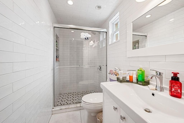 full bath with tile walls, toilet, a stall shower, vanity, and tile patterned floors