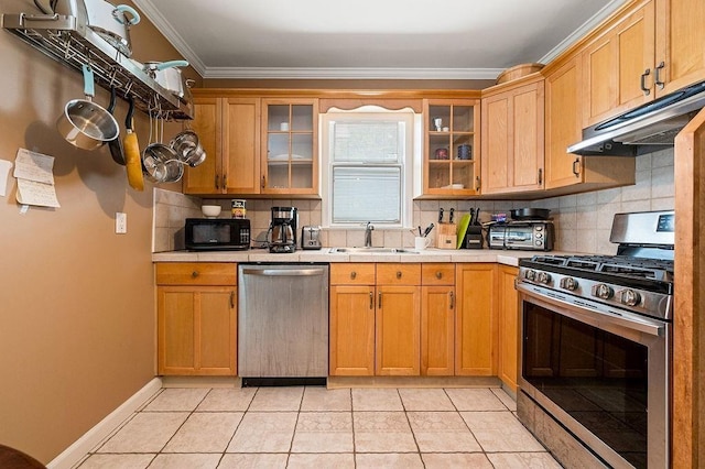 kitchen featuring appliances with stainless steel finishes, glass insert cabinets, under cabinet range hood, and a sink