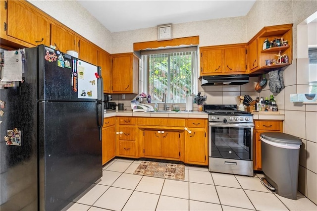 kitchen with brown cabinets, under cabinet range hood, a sink, freestanding refrigerator, and gas range