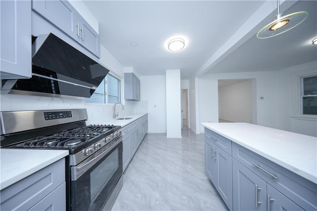 kitchen with range hood, light countertops, gray cabinetry, stainless steel gas stove, and a sink