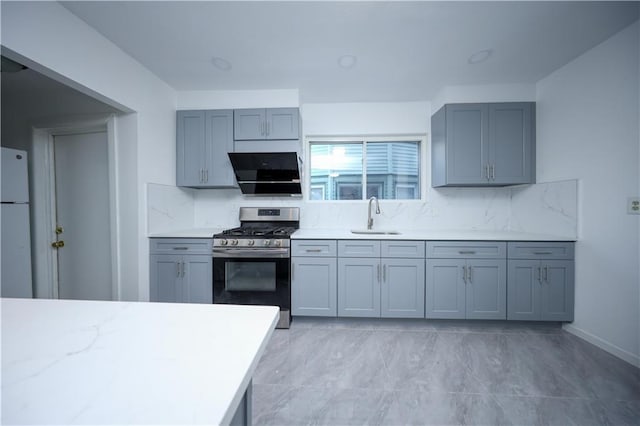 kitchen with a sink, light countertops, stainless steel range with gas stovetop, and freestanding refrigerator