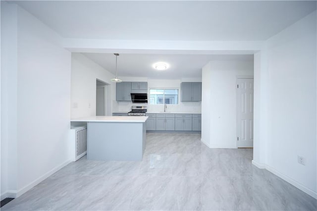 kitchen with stainless steel gas range oven, a peninsula, a sink, light countertops, and gray cabinets