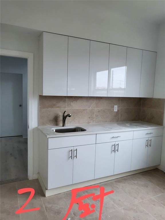 kitchen with decorative backsplash, white cabinetry, and sink