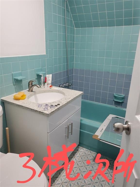 full bathroom with tile patterned floors, toilet, vanity, tile walls, and tiled shower / bath