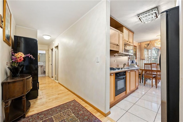 kitchen with light brown cabinets, baseboards, a sink, stainless steel appliances, and light wood-style floors