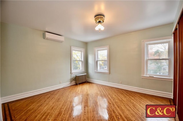 spare room with light hardwood / wood-style floors, a wall unit AC, radiator, and a healthy amount of sunlight