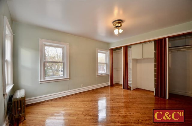 unfurnished bedroom featuring baseboard heating, ceiling fan, light hardwood / wood-style flooring, radiator heating unit, and a closet