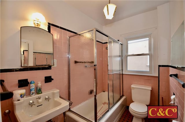 full bathroom with toilet, sink, enclosed tub / shower combo, and tile walls