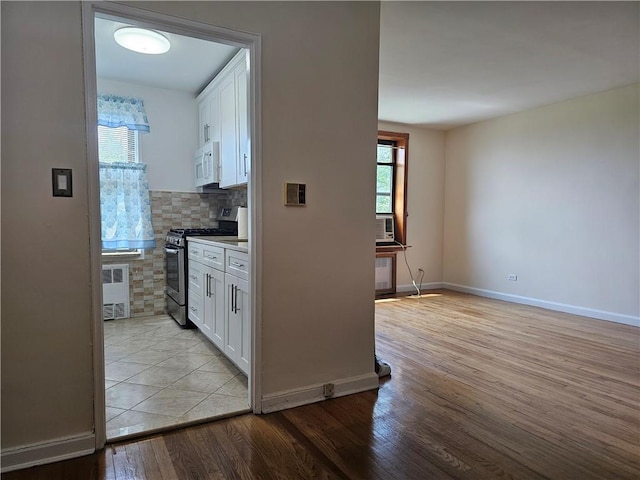 kitchen featuring white cabinetry, radiator heating unit, backsplash, light hardwood / wood-style floors, and stainless steel range with gas stovetop