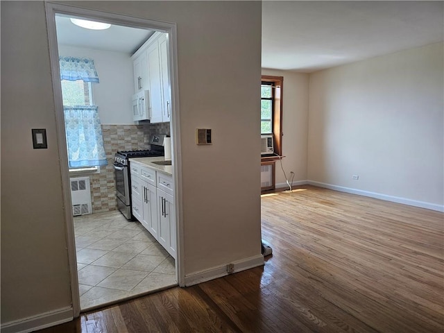 kitchen featuring gas range, backsplash, light hardwood / wood-style floors, and white cabinetry