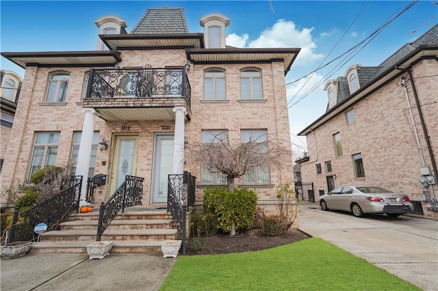 view of front facade with brick siding, concrete driveway, and a balcony