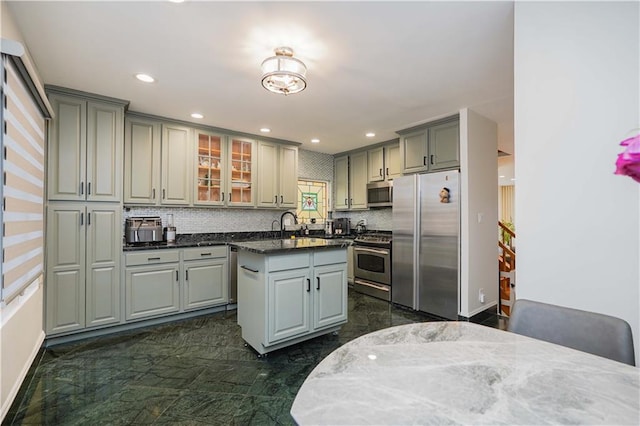 kitchen featuring stainless steel appliances, gray cabinetry, backsplash, dark stone countertops, and a center island