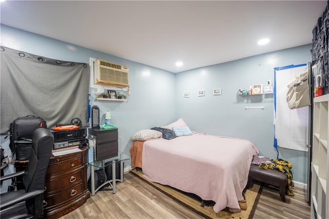 bedroom with a wall mounted AC and light hardwood / wood-style floors