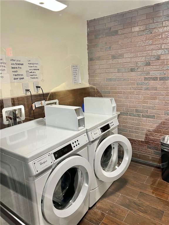 laundry room featuring washing machine and clothes dryer, hardwood / wood-style floors, and brick wall