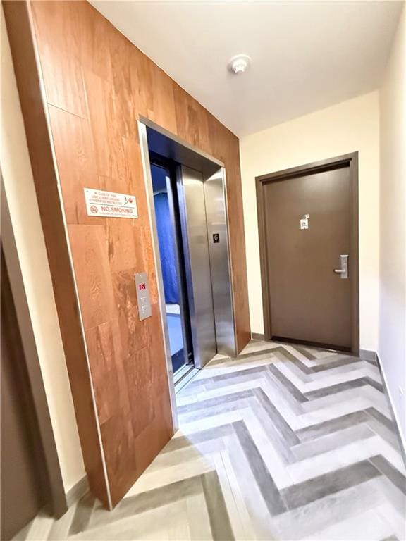 doorway with elevator, light parquet floors, and wooden walls