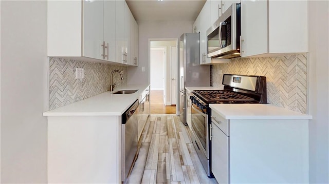 kitchen featuring sink, appliances with stainless steel finishes, white cabinetry, decorative backsplash, and light wood-type flooring