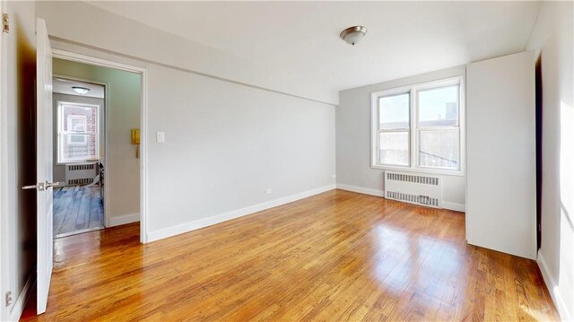 spare room with radiator heating unit and light hardwood / wood-style floors