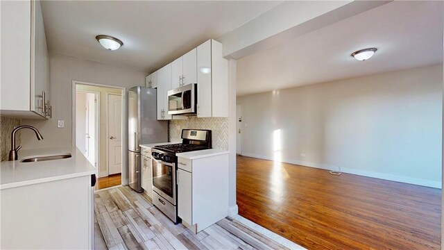 kitchen with sink, stainless steel appliances, decorative backsplash, white cabinets, and light wood-type flooring