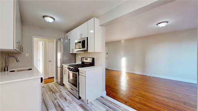 kitchen featuring sink, white cabinets, decorative backsplash, light hardwood / wood-style floors, and stainless steel appliances