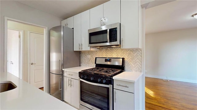 kitchen featuring tasteful backsplash, white cabinetry, light wood-type flooring, and appliances with stainless steel finishes