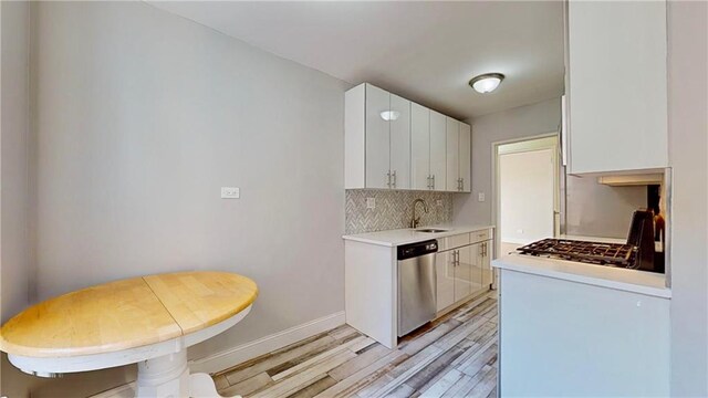 kitchen featuring light wood-type flooring, tasteful backsplash, stainless steel appliances, sink, and white cabinetry