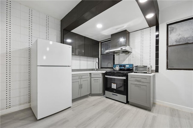 kitchen featuring wall chimney range hood, sink, gray cabinets, white fridge, and stainless steel range with gas stovetop