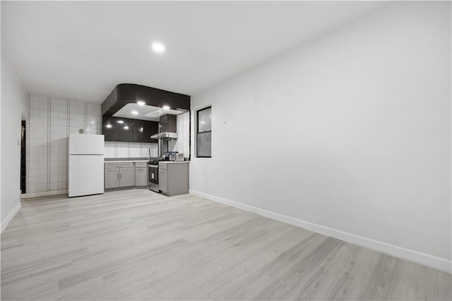 kitchen featuring light hardwood / wood-style flooring, wall chimney exhaust hood, stainless steel gas stove, decorative backsplash, and white fridge