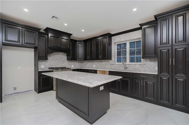 kitchen featuring sink, tasteful backsplash, light stone countertops, a kitchen island, and stainless steel range with gas cooktop