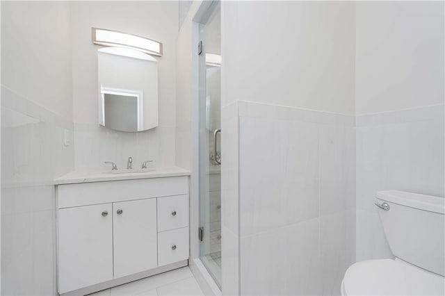 bathroom featuring tile walls, toilet, a stall shower, vanity, and tile patterned flooring