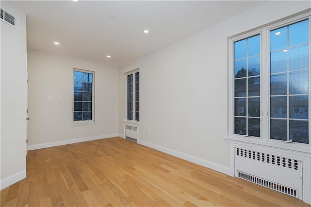 empty room with light wood-style floors, radiator heating unit, visible vents, and baseboards